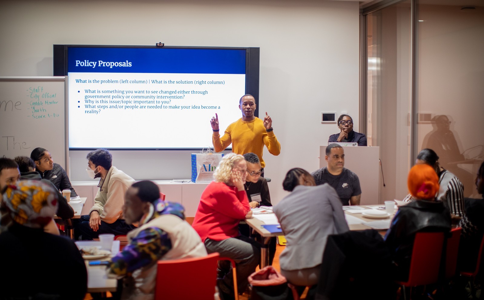 Justice Ambassadors Youth Council Man speaks to room full of people in front of a slide titled Policy Proposals
