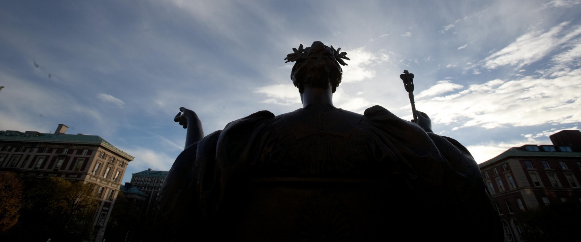 statue of seated woman with outstretched arms against a bright partly cloudy sky