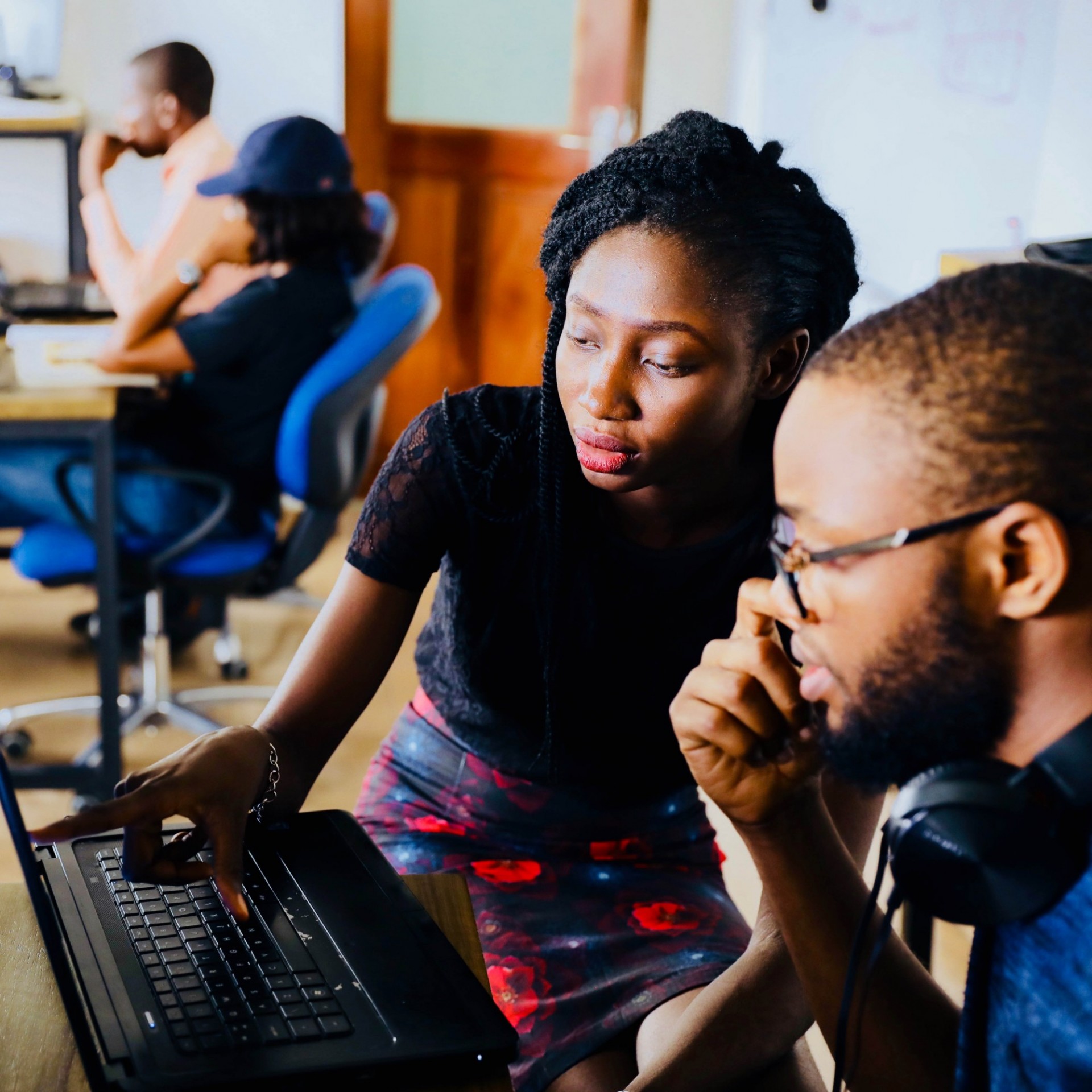 Young woman pointing at a computer screen, explaining something to black man.
